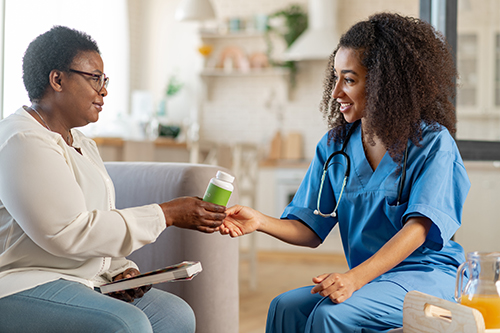 Nursing in blue scrubs handing a woman some vitamins