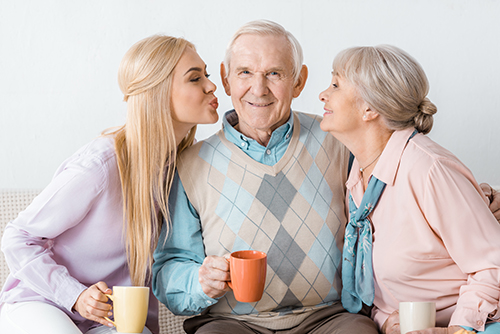 Grandfather wearing plaid vest between his wife and granddaughter blowing him kisses